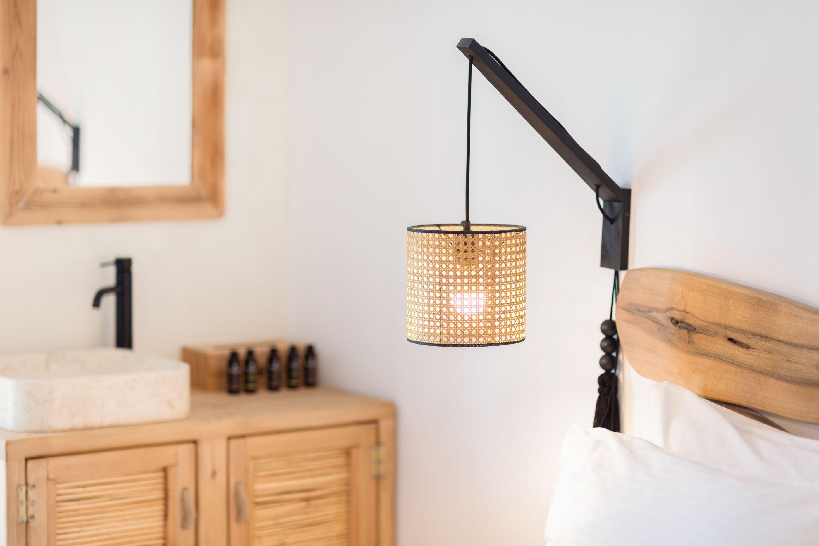 Quarto com cabeceira de madeira, mesa de cabeceira com pia branca e luminária pendente de fibra.