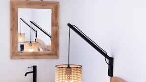 Une salle de bain avec un miroir encadré en bois, un robinet noir et un luminaire tressé.