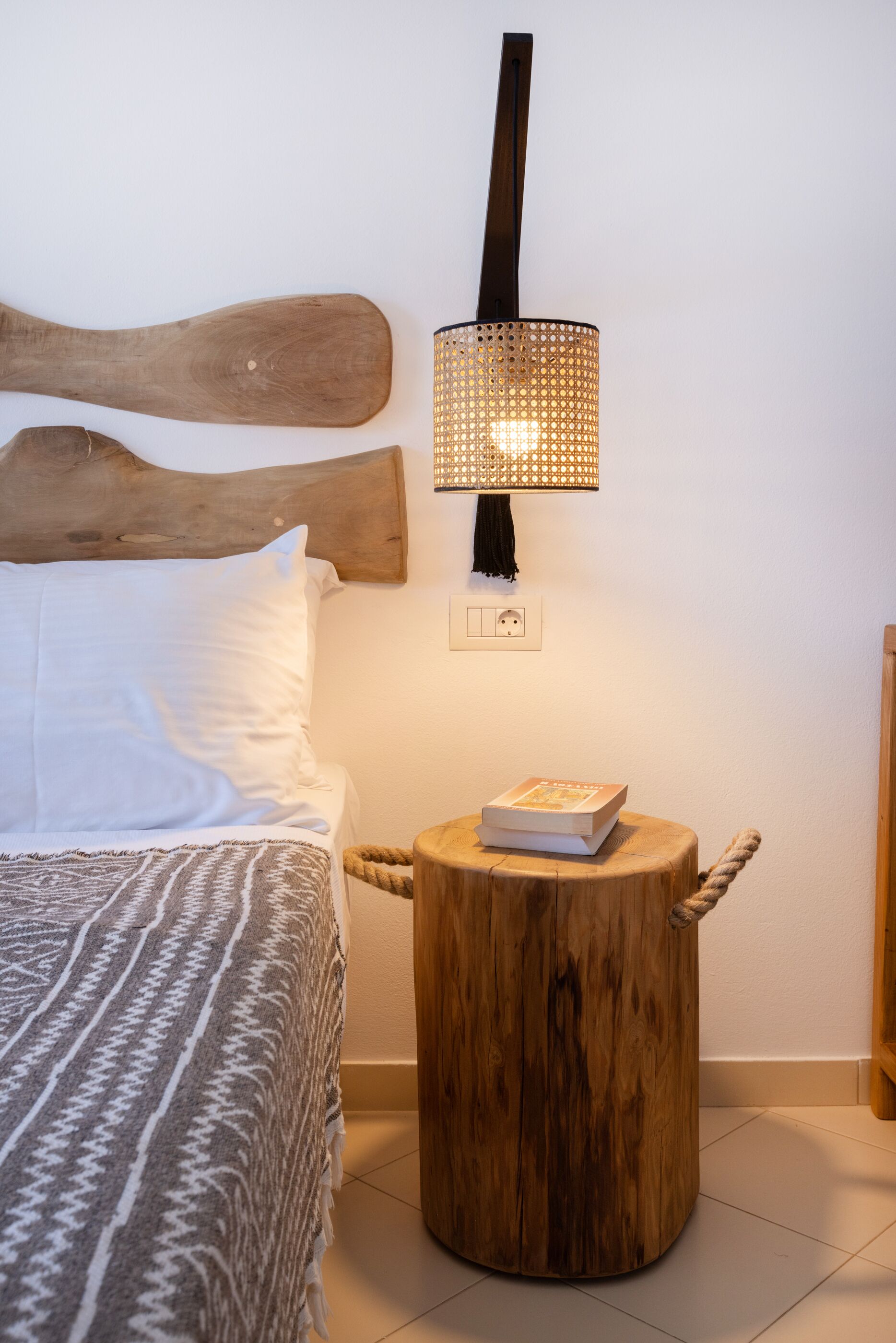 A bed with a patterned blanket, a wooden nightstand with a book, and a wall-mounted lamp.