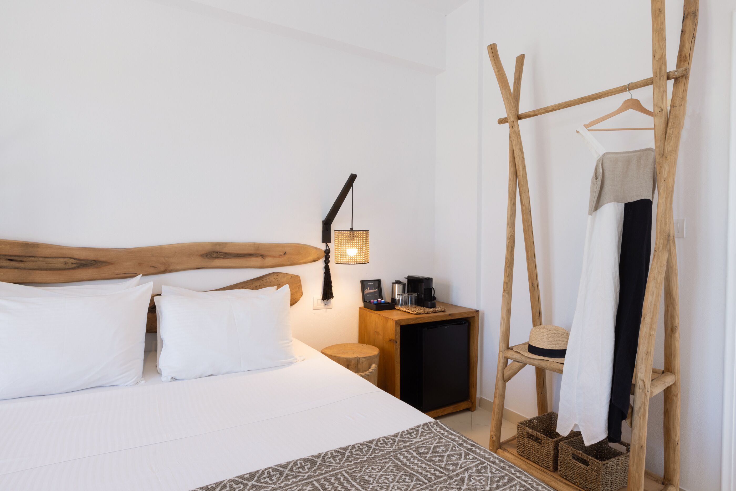 Un dormitorio con cama, mesita de noche con lámpara, un pequeño armario de madera y un perchero.