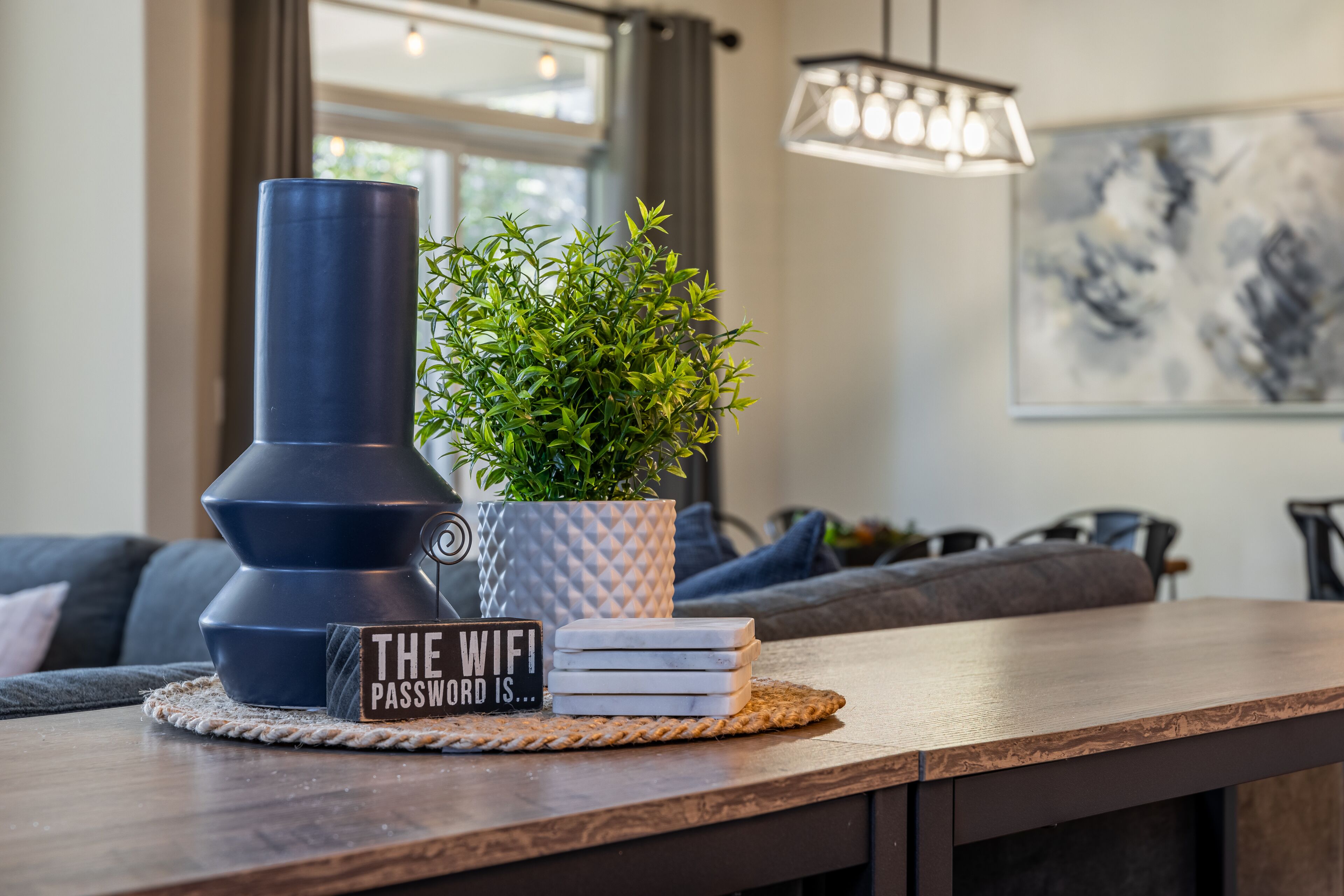 Una mesa de madera con una planta en maceta, un jarrón decorativo y un letrero que dice "THE WIFI PASSWORD IS...".