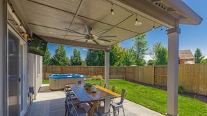 A covered patio with a wooden table and chairs, a ceiling fan, and a hot tub.
