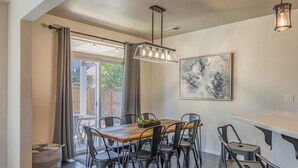 A dining area with a wooden table, black chairs, a hanging light fixture, and a painting on the wall.