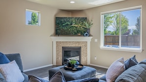 A living room with a fireplace, a large window, and a television mounted above it.