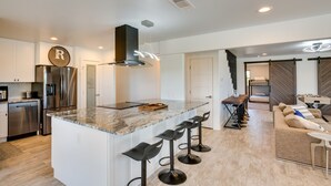 A modern kitchen with a central island, bar stools, and a dining area with a sofa and table. - Cozy Interior + Lake View: McKinney Ranch Home! (McKinney)