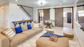 A modern living room with a sofa, ottoman, and a foosball table. - Cozy Interior + Lake View: McKinney Ranch Home! (McKinney)
