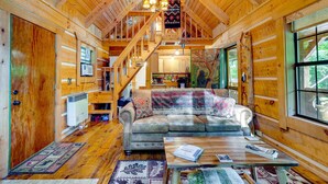 A cozy log cabin interior with a wooden staircase, a sofa, and a dining table. - Cozy Log Cabin on 11 Acres: 3 Mi to Cherokee Lake! (Bean Station)
