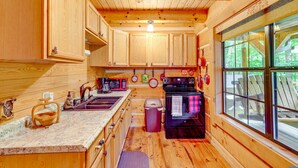 A wooden cabin kitchen with a large window, wooden cabinets, a stove, and a sink. - Cozy Log Cabin on 11 Acres: 3 Mi to Cherokee Lake! (Bean Station)