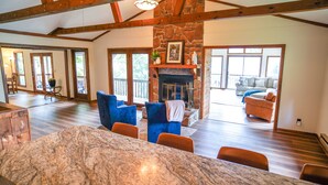 A spacious living room with a stone fireplace, a large wooden dining table, and a cozy seating area with blue and orange chairs.