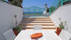 A staircase leading to a terrace with a view of the sea, white furniture, and potted plants.