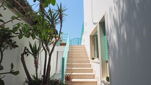 A narrow alleyway with a staircase leading to a building with a white exterior and green shutters.