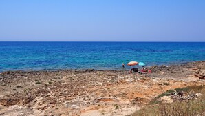 A rocky beach with clear blue sea, a few people, and a beach umbrella.