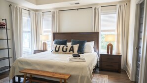 Een keurig opgemaakte slaapkamer met een groot bed, twee nachtkastjes, een bankje en een kledingkast.