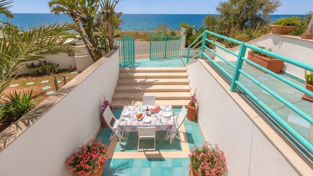 Eine Terrasse mit Esstisch und Blick auf die Küste.