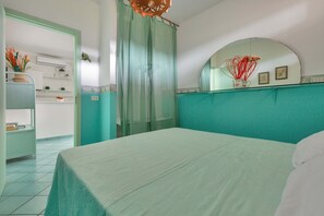 A bedroom with a bed, a bathroom with a shower curtain, and a kitchen area visible through an open door.