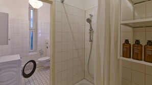 Un bagno con doccia, servizi igienici e lavandino. Prodotti per la cura della persona su uno scaffale.