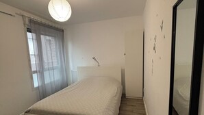 Ett sovrum med en säng, ett fönster med gardiner, en taklampa och en spegel på väggen.