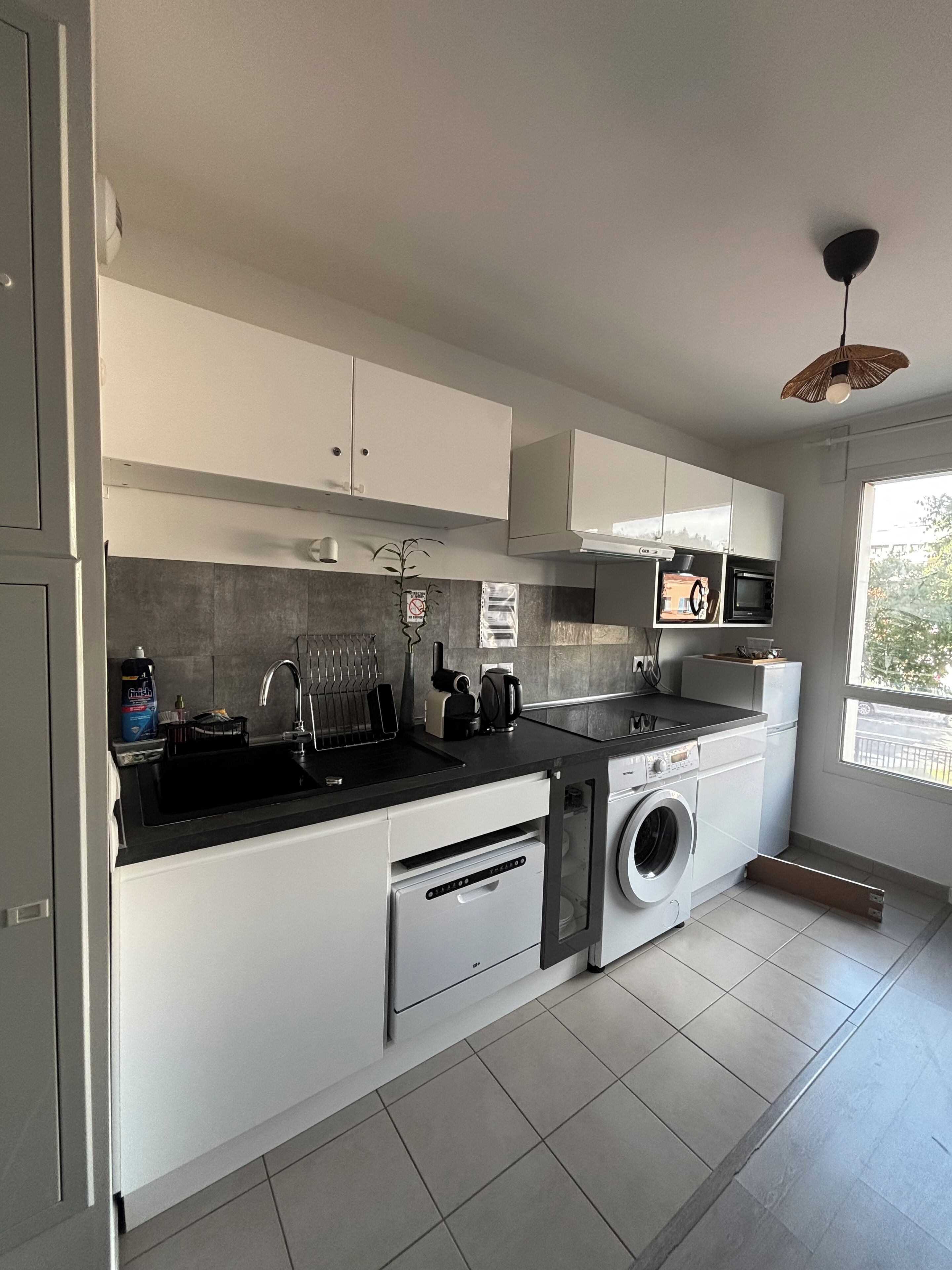 Une cuisine moderne avec des meubles blancs, un plan de travail noir, un lave-linge encastré et un four à micro-ondes.