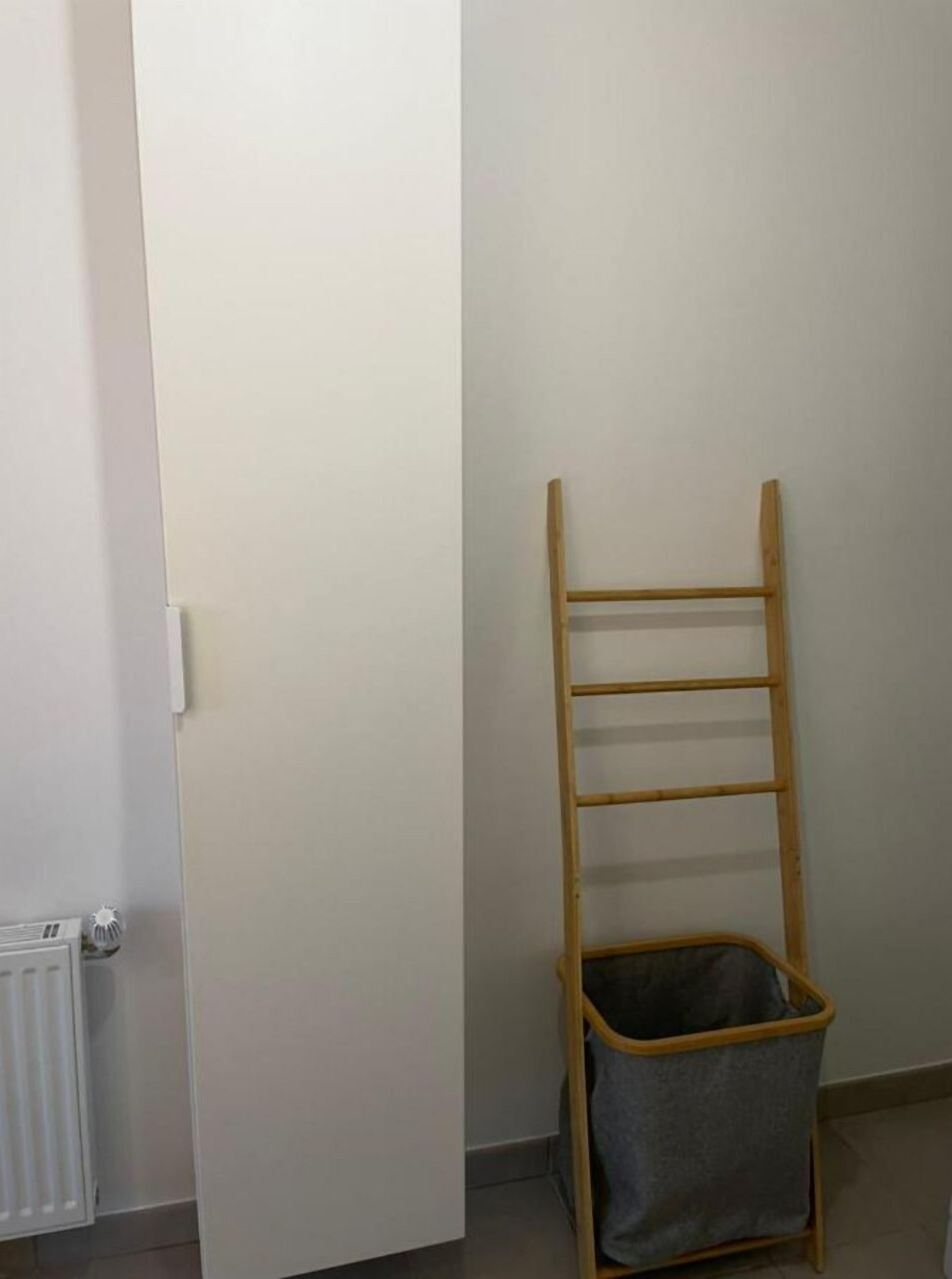 Ein Zimmer mit einer weißen Tür, einem Heizkörper und einer Holzlaufleiter mit Korb am unteren Ende.