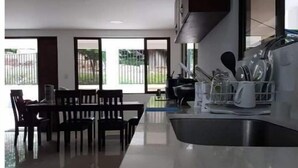 Una cocina moderna con una isla grande, zona de comedor con sillas y vistas al exterior a través de ventanas amplias.