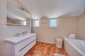 Ein modernes Badezimmer mit großem Spiegel, zwei Waschbecken, einer Badewanne und einem kleinen Fenster.