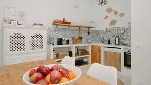 A modern kitchen with white cabinetry, a wooden dining table, and a fruit bowl. - Casa Familia - House for 4 (Sa Pobla)