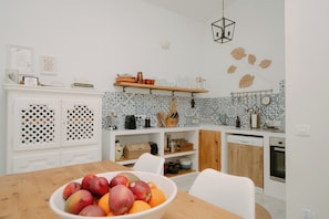 A modern kitchen with white cabinetry, a wooden dining table, and a fruit bowl.