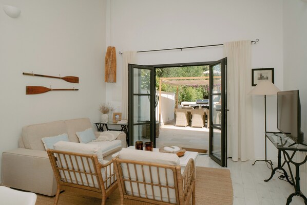 A room with a sofa, two wicker chairs, a TV stand, and a glass door leading to an outdoor area.