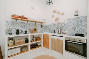 A kitchen with white cabinets, a wooden shelf, a microwave, a toaster, and a stove.