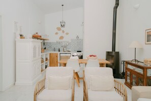 A modern living room with a dining area, white furniture, a fireplace, and a kitchen in the background.