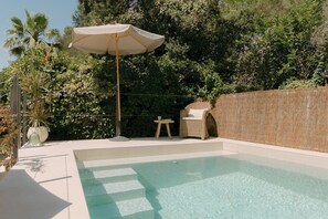 A swimming pool with a sun umbrella, a wicker chair, and a small table.