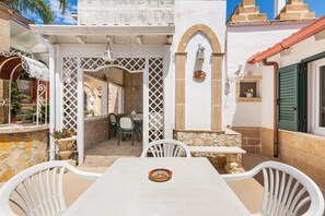 Un patio con una mesa y sillas, un área de estar techada y vista a la calle.