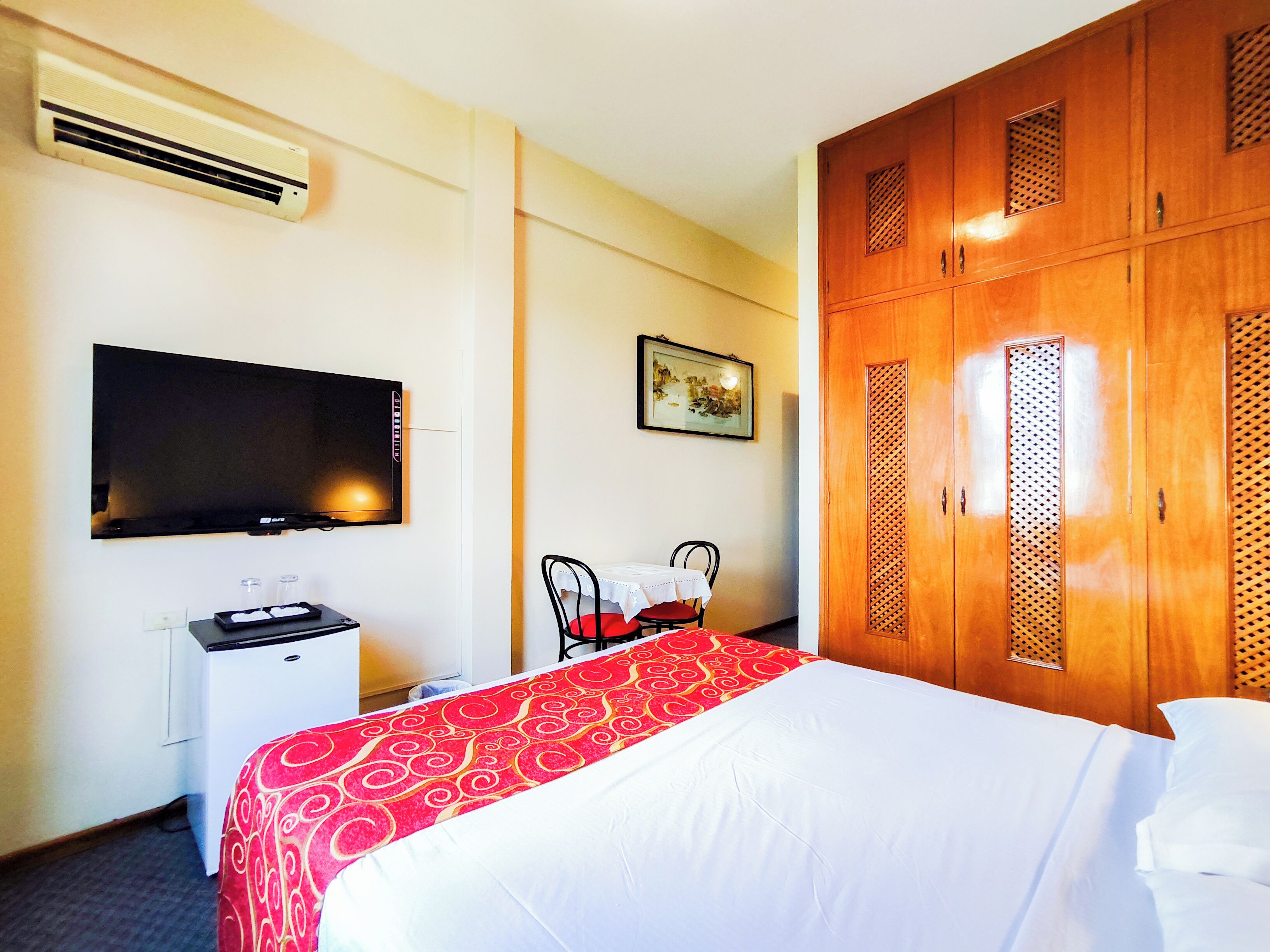 A hotel room with a bed, a desk, a chair, a TV, and a wardrobe.