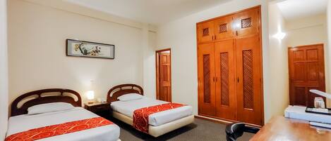 A hotel room with two beds, a desk, a chair, a wardrobe, and a framed picture on the wall.