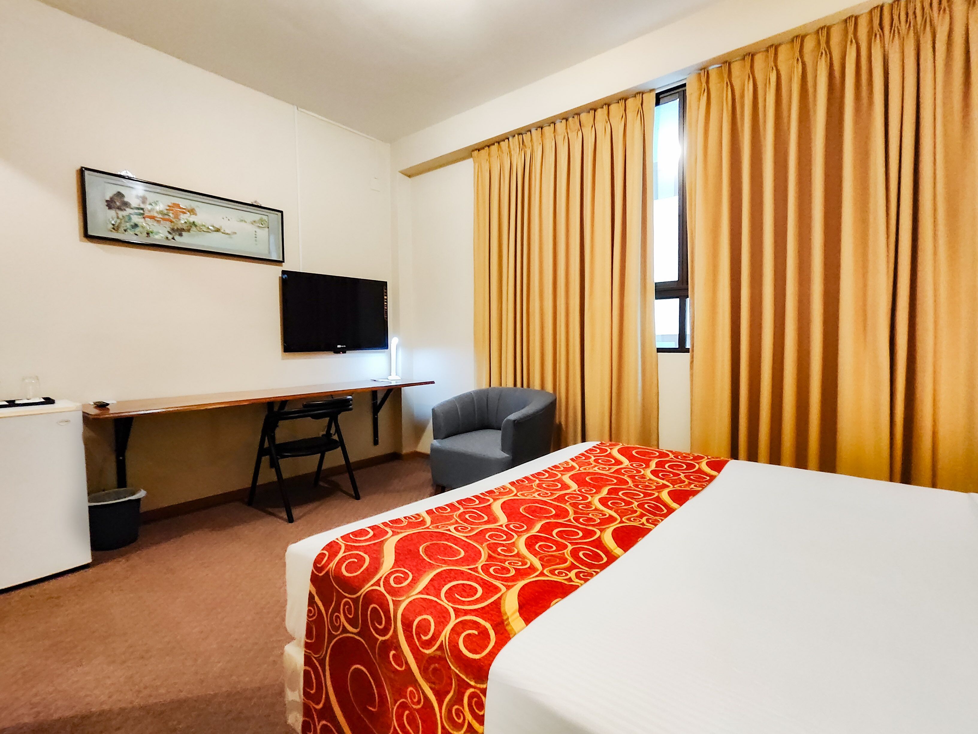 Una habitación de hotel con una cama, un escritorio, una silla, un televisor y una ventana con cortinas.
