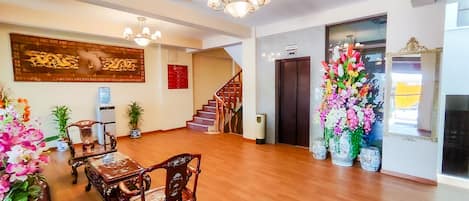 A spacious lobby with wooden flooring, a staircase, a reception desk, and a large floral arrangement.