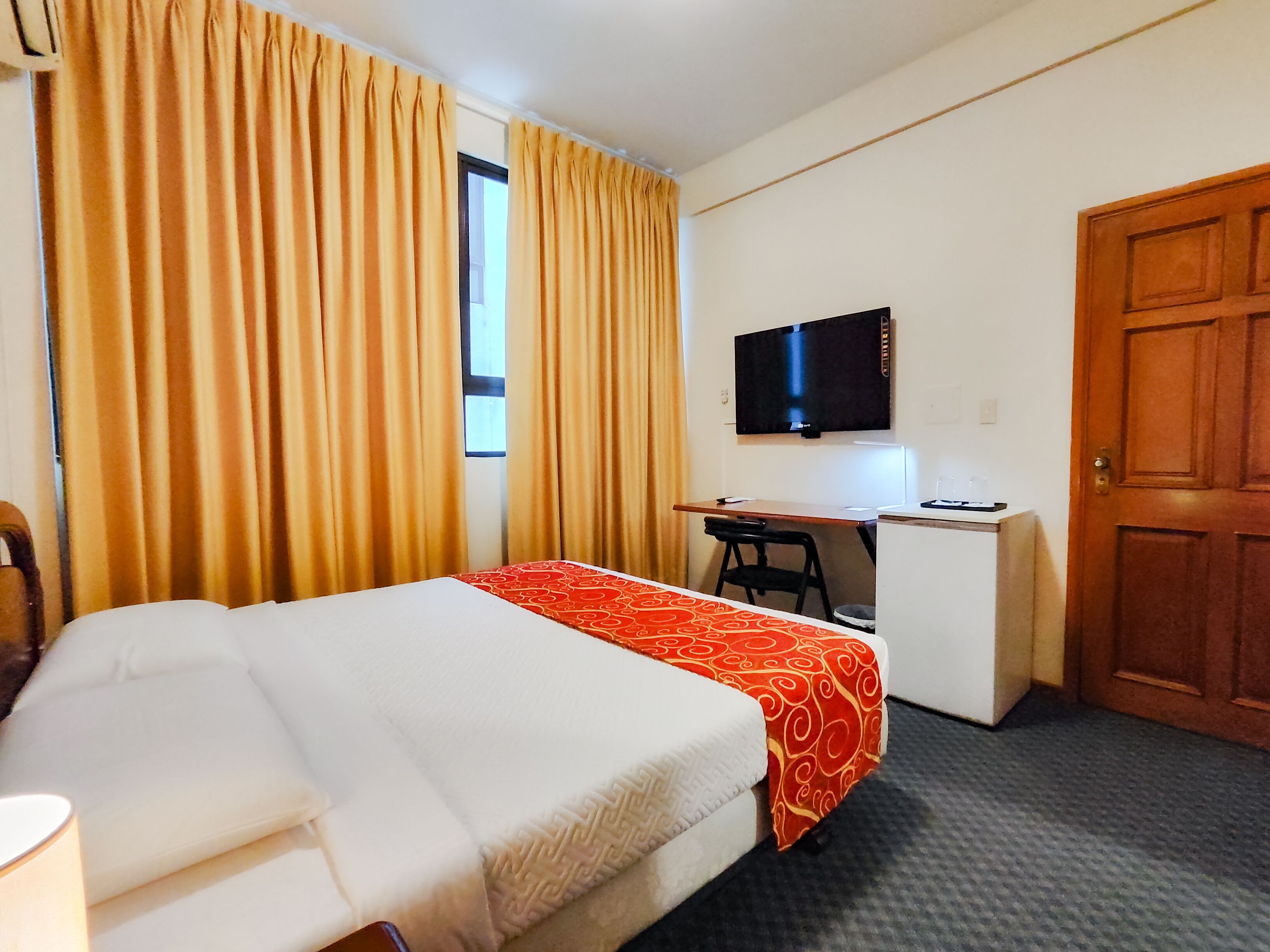 A hotel room with a bed, a desk, a chair, a television, and a wardrobe.