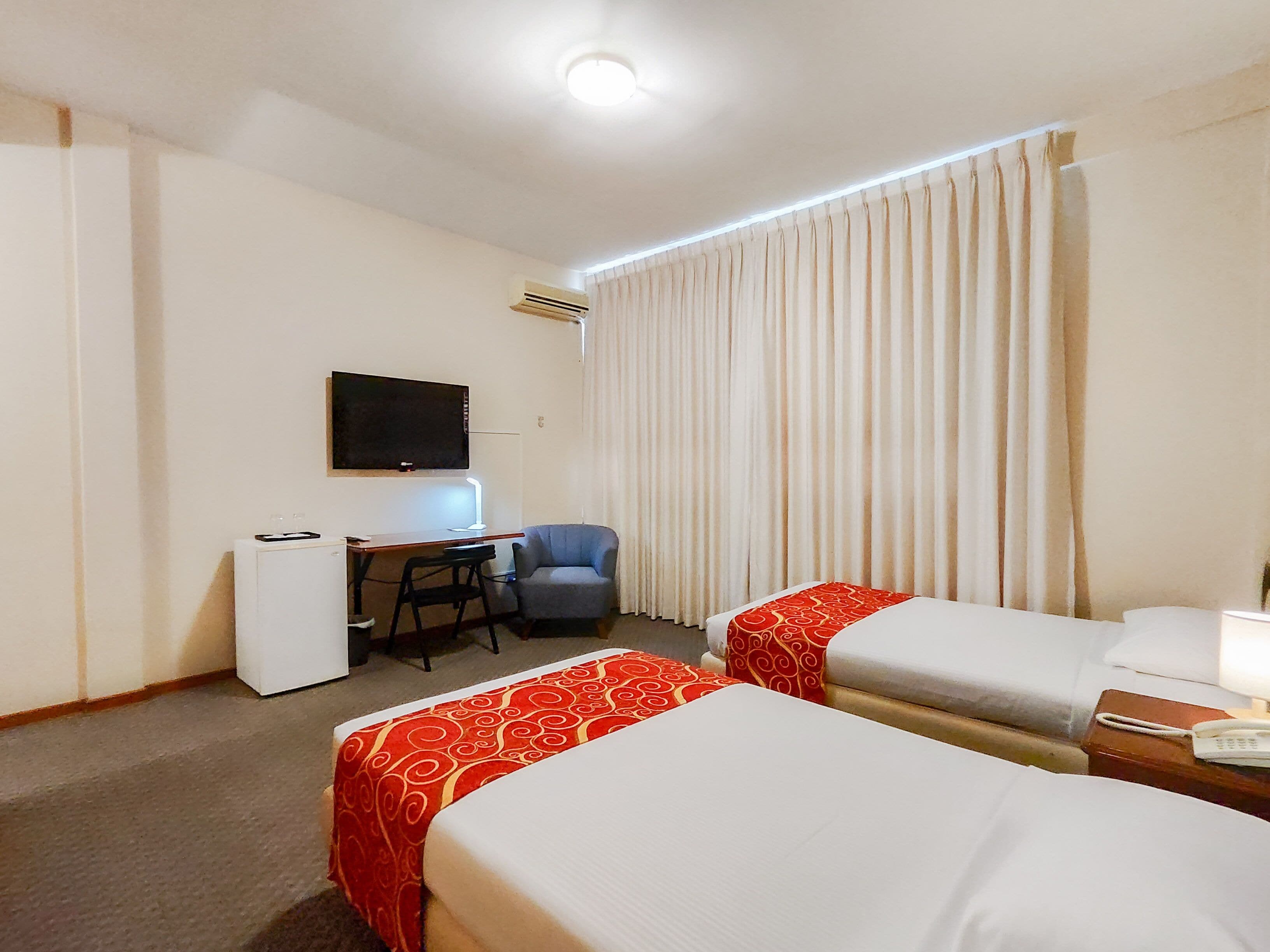 A hotel room with two beds, a desk, a chair, a TV, and a phone.