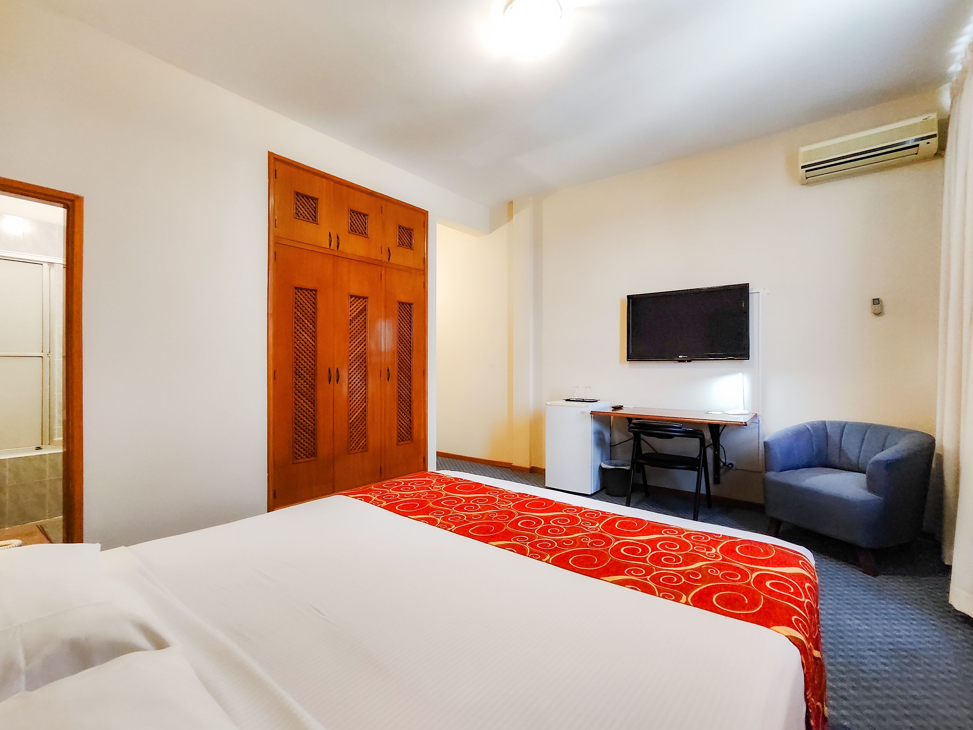 A hotel room with a bed, a desk, a chair, a television, and a wardrobe.