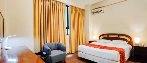 A hotel room with a bed, a desk, a chair, and a window with curtains.
