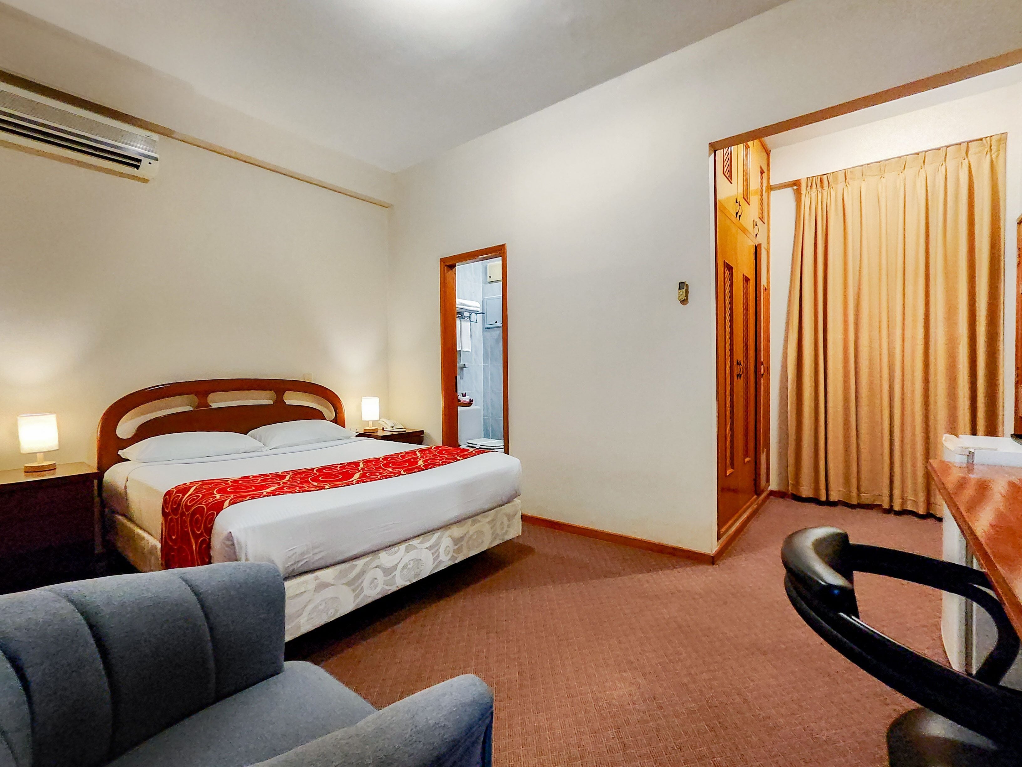 A hotel room with a bed, bedside table, lamp, chair, and a door leading to a bathroom.