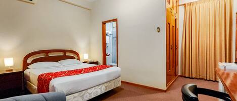 A hotel room with a bed, bedside table, lamp, chair, and a door leading to a bathroom.