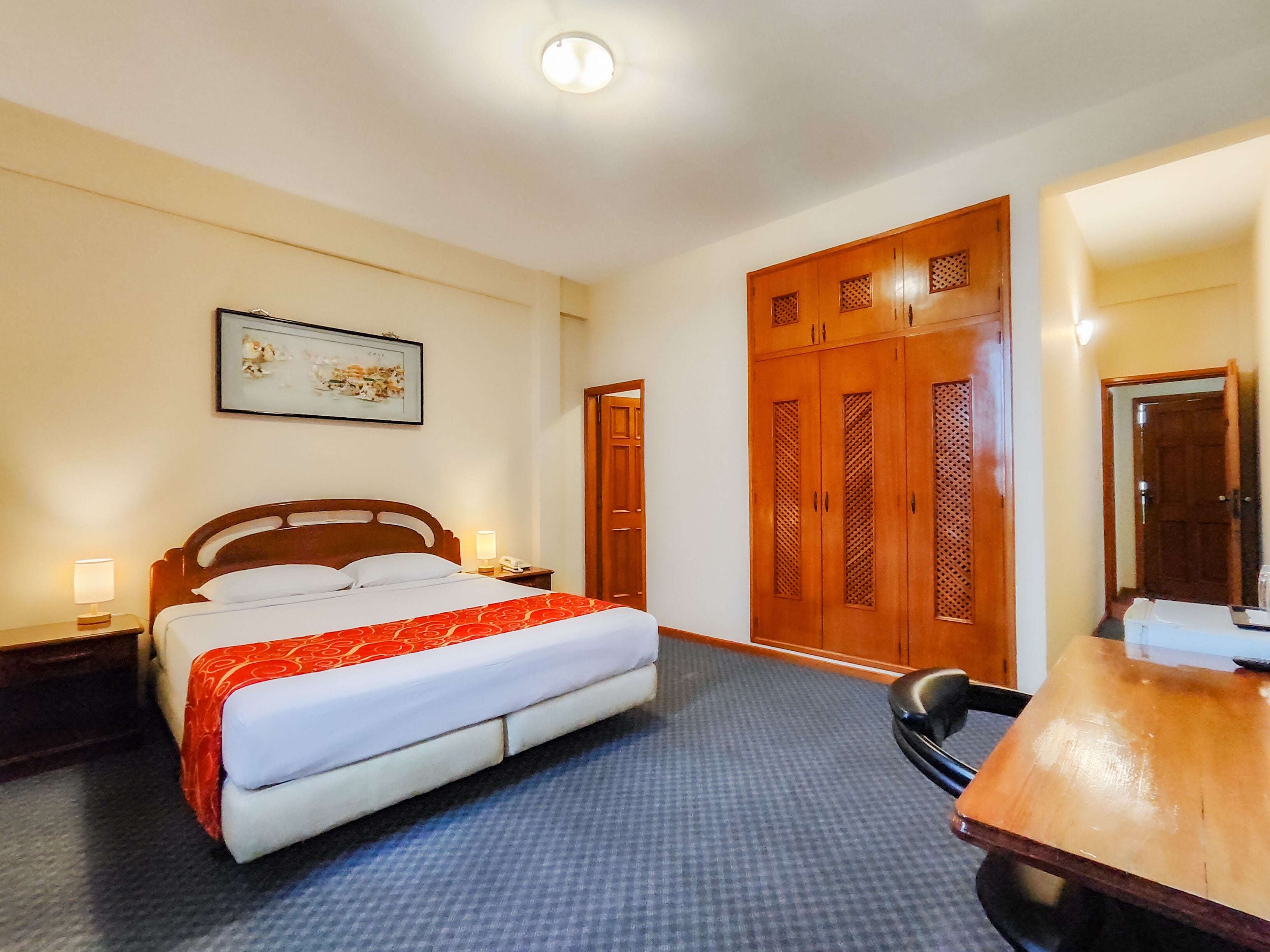 Ein Hotelzimmer mit Bett, Schreibtisch, Stuhl, Kleiderschrank und einem gerahmten Bild an der Wand.