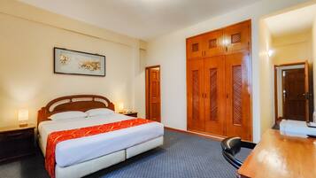 Una habitación de hotel con cama, escritorio, silla, armario y un cuadro en la pared.