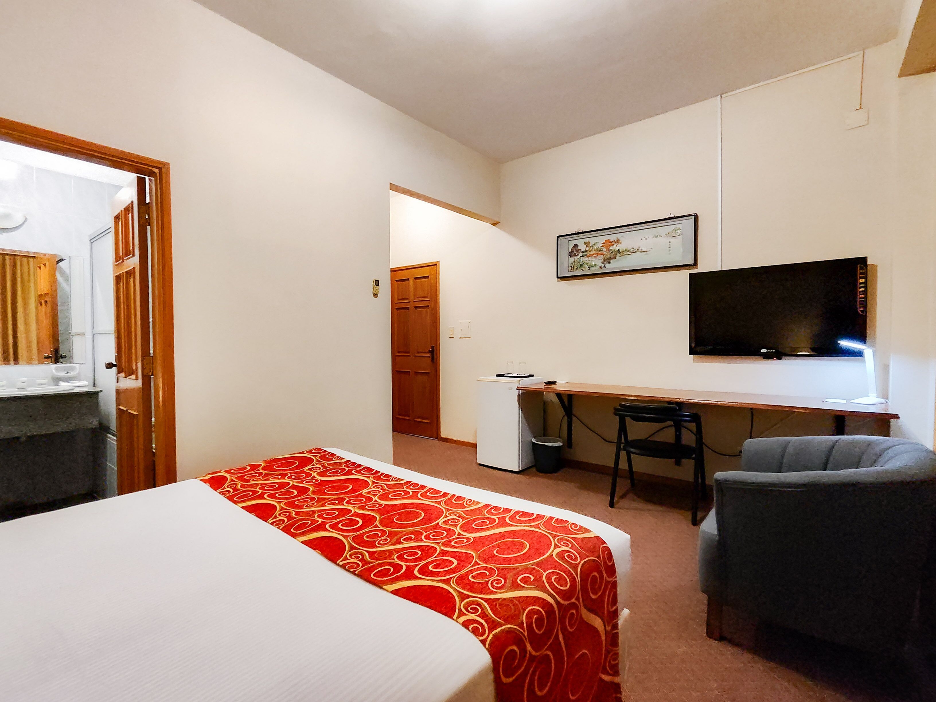 Una habitación de hotel con una cama, un escritorio, una silla, un televisor y una pequeña kitchenette.