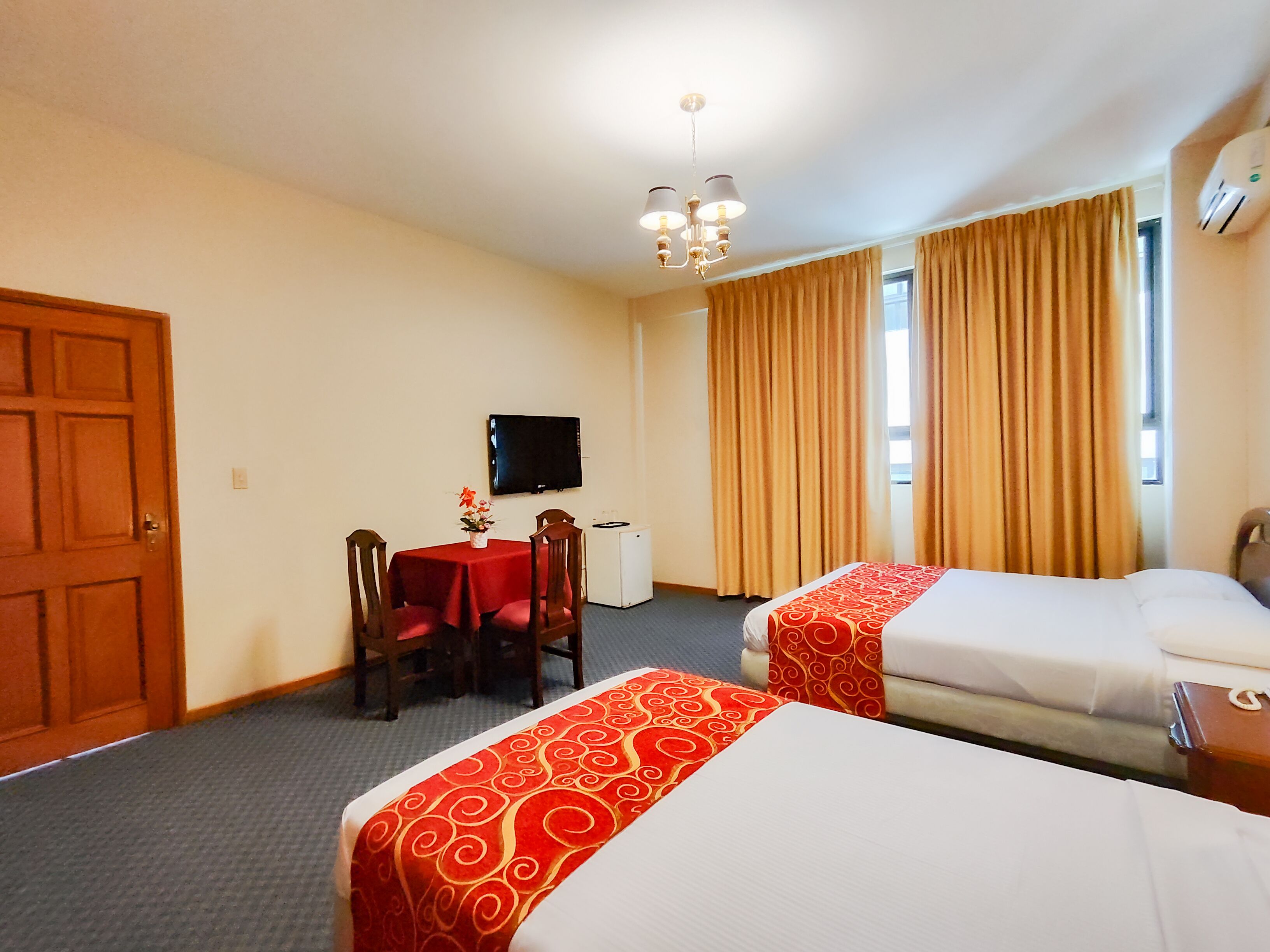 A hotel room with two beds, a desk with a chair, a television, and a window with curtains.