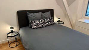 A bedroom with a bed, two bedside tables, a nightstand, a window, and a white wall. - Bel Appartement Avec Parking au Coeur de Reims (Reims)