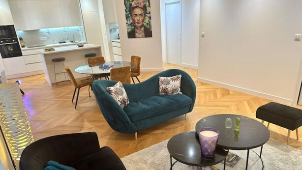 A modern living room with a teal sofa, black armchair, and a small round table with a candle. A dining area with a white table and chairs is visible in the background. - Bel Appartement Avec Parking au Coeur de Reims (Reims)