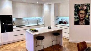 A modern kitchen with white cabinetry, a marble backsplash, a built-in oven, and a small island with stools. - Bel Appartement Avec Parking au Coeur de Reims (Reims)