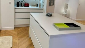 A modern kitchen with white cabinetry, a marble backsplash, and a herringbone wood floor. - Bel Appartement Avec Parking au Coeur de Reims (Reims)